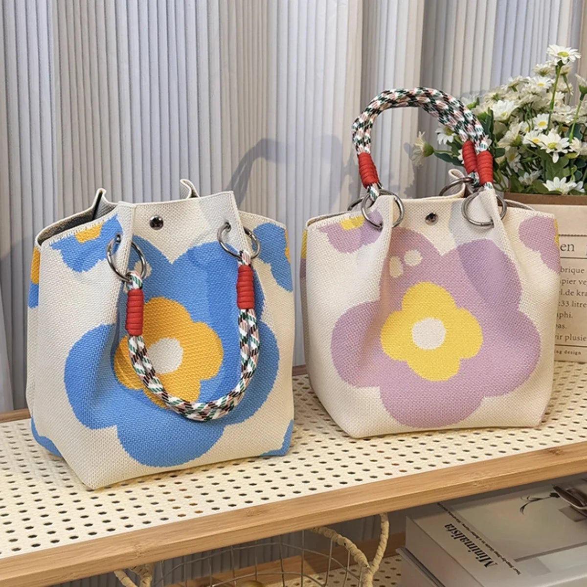 A light beige knitted bucket handbag with purple and yellow floral embroidery and red and white braided handles.
