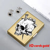 A gold card holder featuring a detailed black and white skull design, with two silver stud earrings nearby.