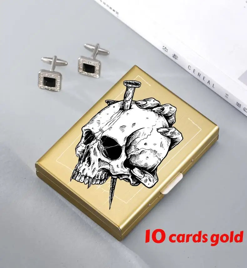 A gold card holder featuring a detailed black and white skull design, with two silver stud earrings nearby.