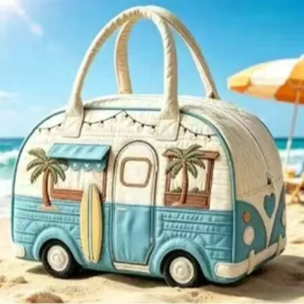 A light blue quilted travel duffle bag with a handle and palm tree design is resting on a sandy beach.