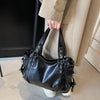 A black leather tote bag with a strap is held by a person in a light-colored suit jacket.