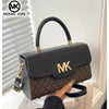 A black Michael Kors letter square crossbody bag with gold hardware resting on a light surface.
