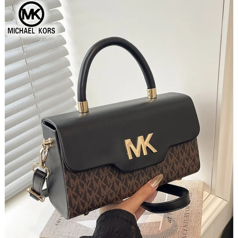 A black Michael Kors letter square crossbody bag with gold hardware resting on a light surface.
