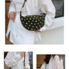 A woman holds a dark olive green faux suede hobo crossbody bag with gold rivet accents against a white shirt.