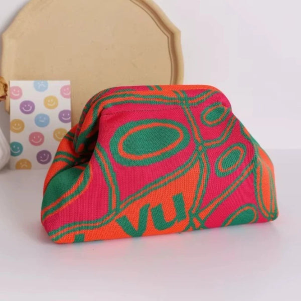 A bright pink and orange knitted clip bag with an olive green pattern resting on a white surface.