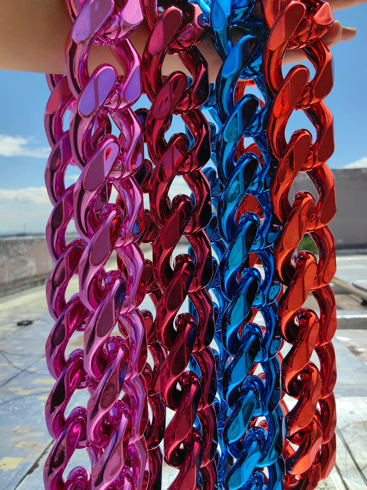 A close-up of a chunky gold acrylic Cuban link necklace featuring vibrant pink, blue, and red colored links.