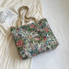 A floral patterned bohemian corduroy tote bag resting on a white surface next to a light-colored garment.