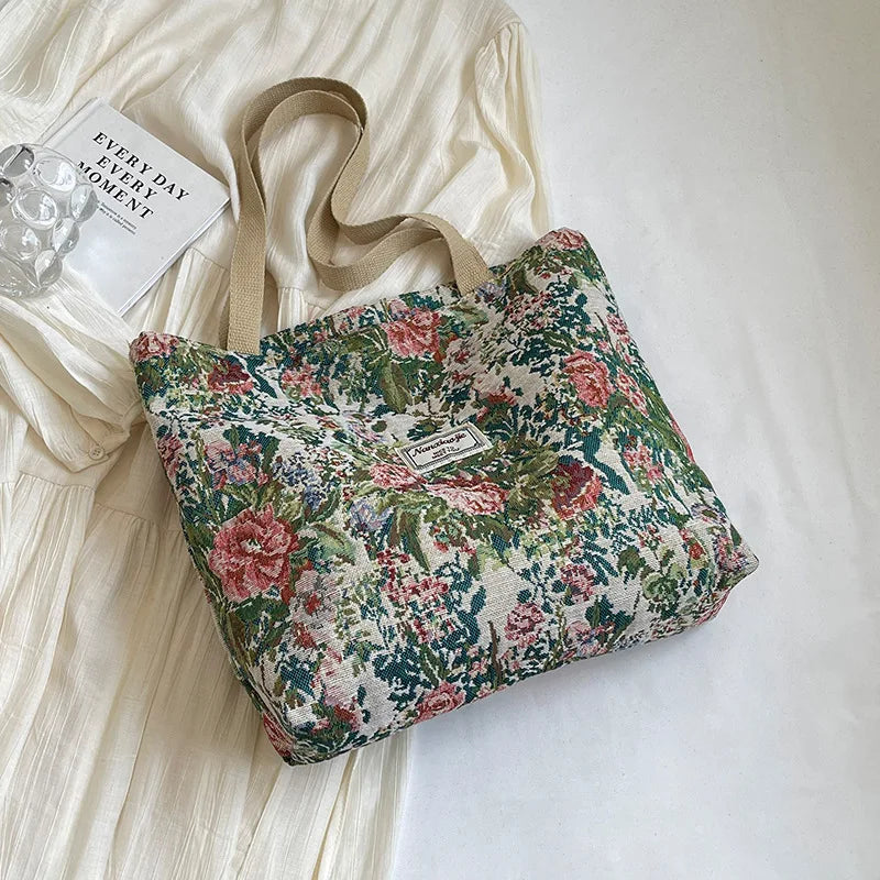 A floral patterned bohemian corduroy tote bag resting on a white surface next to a light-colored garment.