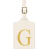 Étiquette de bagage beige en cuir rectangulaire avec un G brodé en or et une pince métallique argentée.