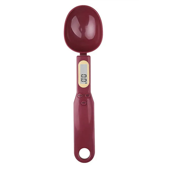 A maroon digital kitchen scale with a round, glossy measuring spoon attachment.