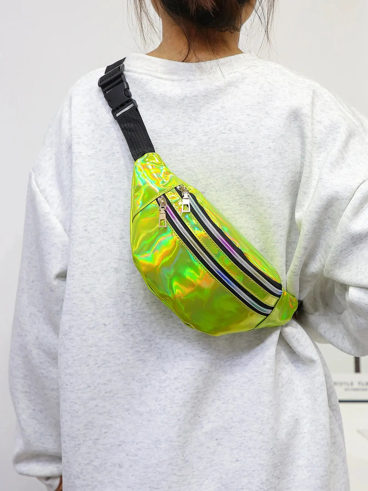 A bright holographic sequin waist bag with black stripes and an adjustable strap worn on a gray sweatshirt.