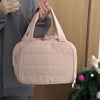 Eine hellrosa, gesteppte portable Make-up-Organizer-Tasche wird von einer Person vor einem Holz-Hintergrund gehalten.