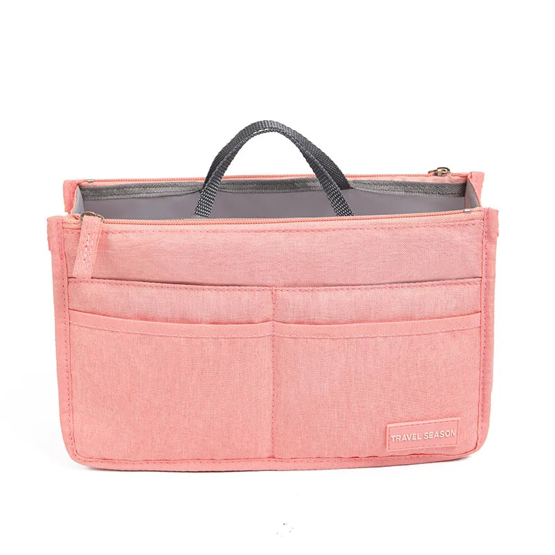 A pink fabric handbag with a gray lining and a black handle, featuring multiple internal pockets.