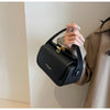 A hand holds a black textured leather shoulder bag against a light wall.