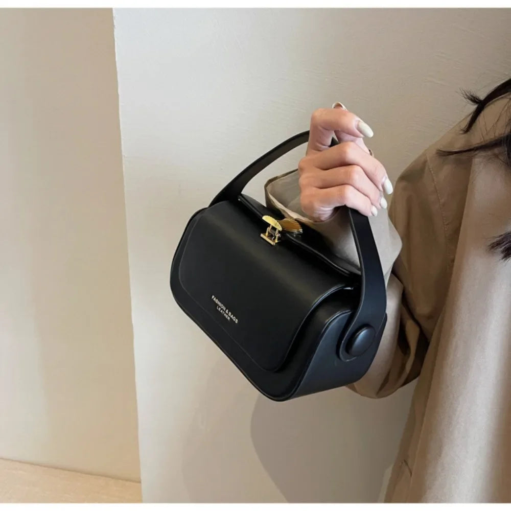 A hand holds a black textured leather shoulder bag against a light wall.