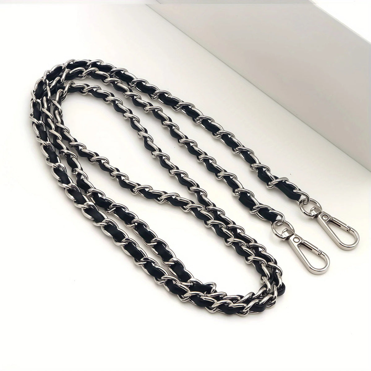 Nahaufnahme eines schwarzen und silbernen verstellbaren Metall-Crossbody-Gürtels einer Tasche auf einer weißen Oberfläche.