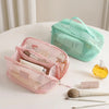 A pink mesh cosmetic organizer pouch and a mint green zippered pouch are displayed on a white surface.