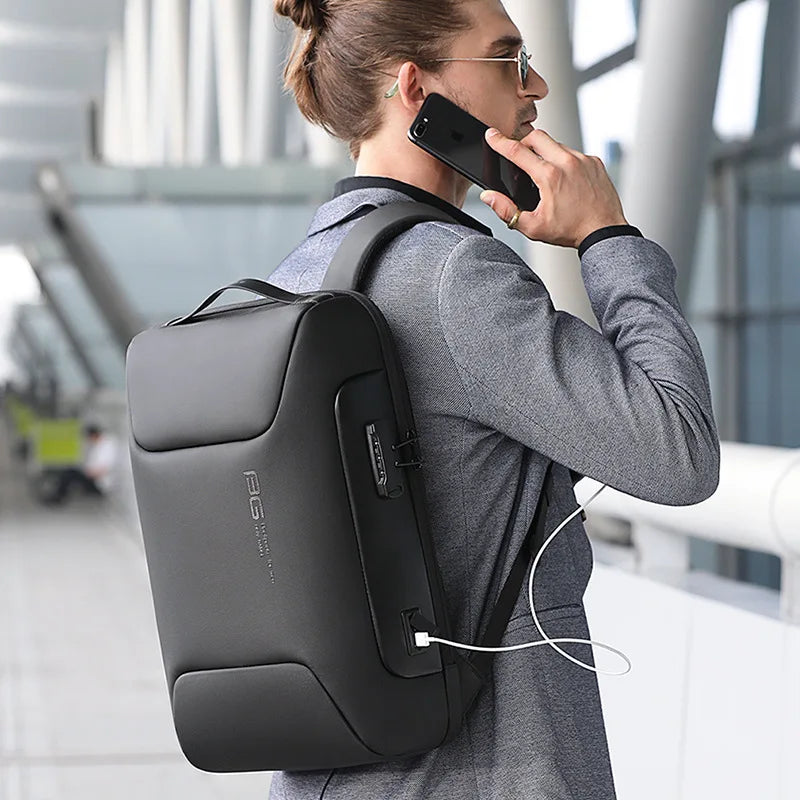 A person is holding a black anti-theft waterproof laptop backpack with a USB charging port.