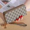Cartera con cremallera de imitación de cuero beige y cadena dorada, sobre una superficie de madera junto a papel impreso.