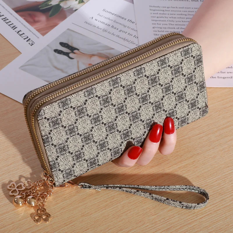 Cartera con cremallera de imitación de cuero beige y cadena dorada, sobre una superficie de madera junto a papel impreso.