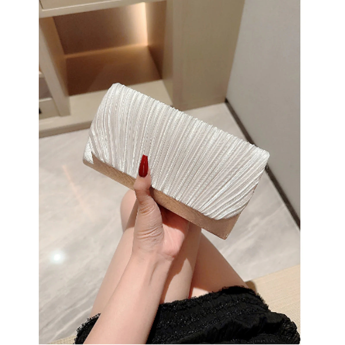 A close-up of a white pleated luxury chain shoulder clutch bag held by a hand.