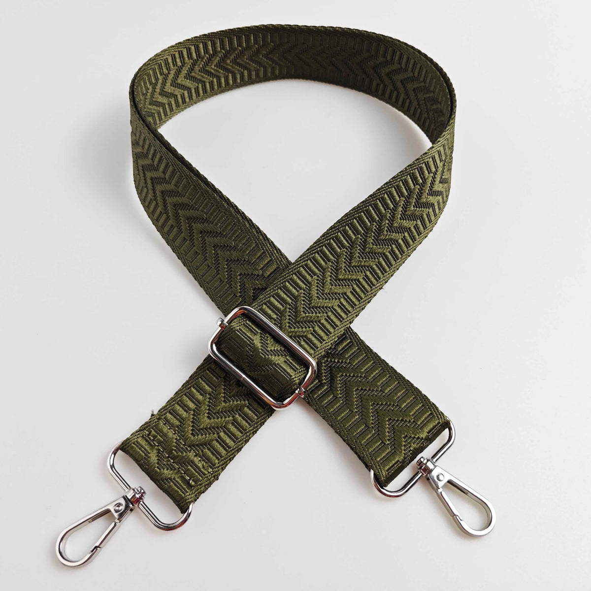 A wide, olive green adjustable handbag strap featuring an arrow jacquard pattern.