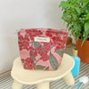 A pink floral patterned cosmetic pouch resting on a light-colored stool next to a potted green plant.