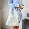 A woman holds a white knitted tote bag with blue floral embroidery against a light background.