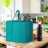 A teal reusable foldable grocery tote bag shown with dimensions and context on a wooden surface.