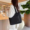A woman holds a black large capacity waterproof canvas tote bag in an indoor setting.