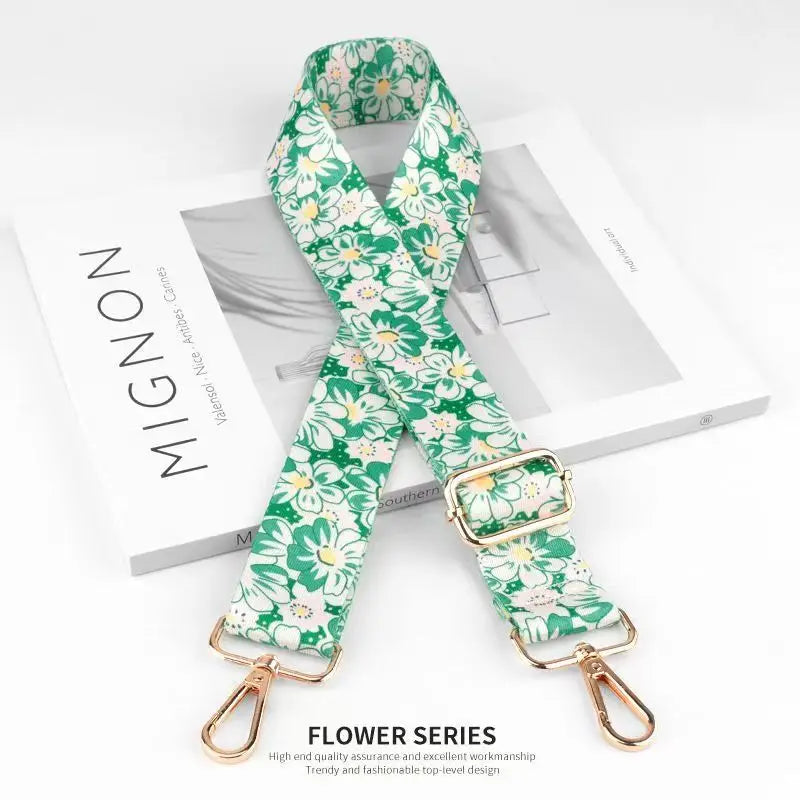 A green floral patterned nylon bag strap with a gold buckle is displayed on a white background.