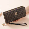 A dark brown monogrammed double zipper wallet with a gold logo and leather strap resting on a light background.