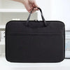 A black laptop sleeve with a handle is being held by a hand, shown on a white surface.