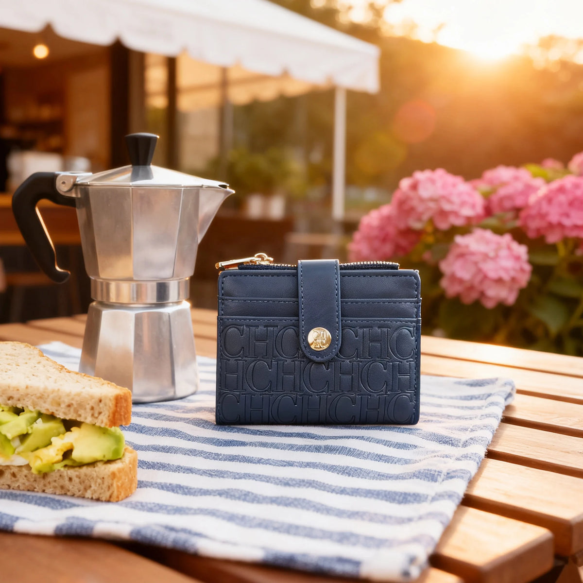 A navy blue classic square folding wallet resting on a striped cloth next to a sandwich and a silver milk frother.