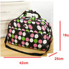 A black duffel bag with pink, green, and white polka dots is shown on a wooden surface.