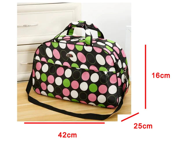 A black duffel bag with pink, green, and white polka dots is shown on a wooden surface.