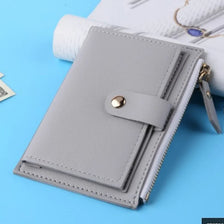 A light gray leather compact wallet with a zipper closure and a card holder is shown on a blue background.