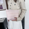 A light pink quilted cosmetic travel bag is held by a person wearing a cream knit sweater.