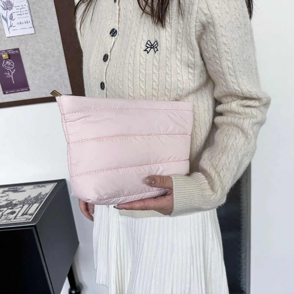 A light pink quilted cosmetic travel bag is held by a person wearing a cream knit sweater.