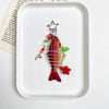 A red and pink simulation fish keychain with a silver charm and a red star charm displayed on a white square plate.