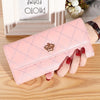 A pink quilted wallet with a gold crown buckle is held by a hand on a wooden surface.