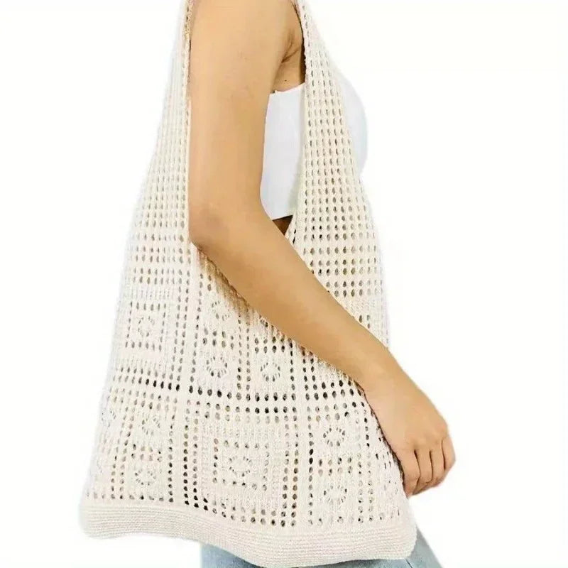 A close-up of a cream-colored knitted shoulder bag for women being worn on the arm.