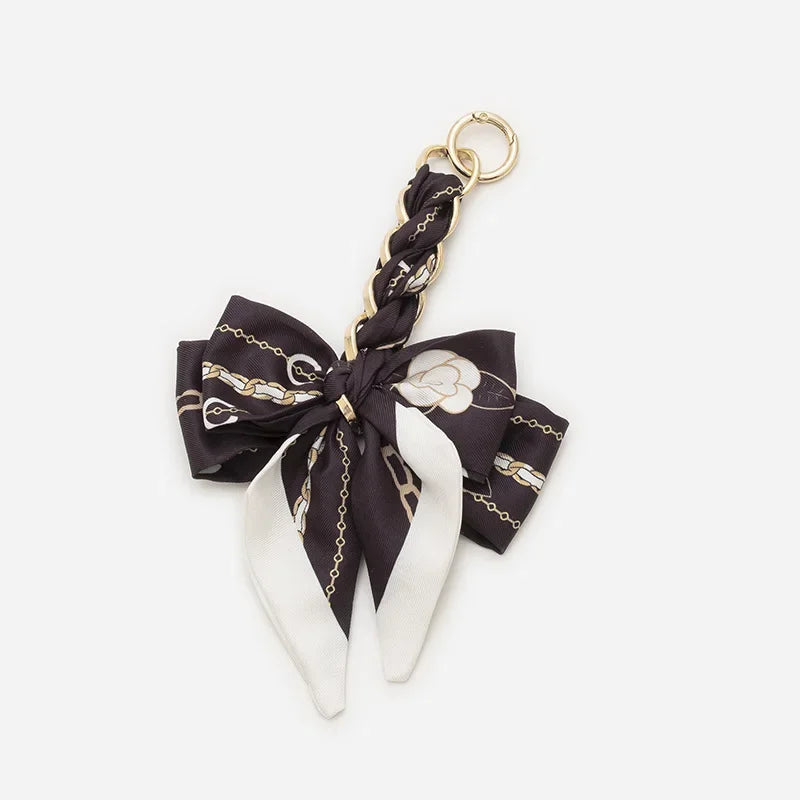 A black and white patterned bow bag chain strap extension with a gold-toned clasp.