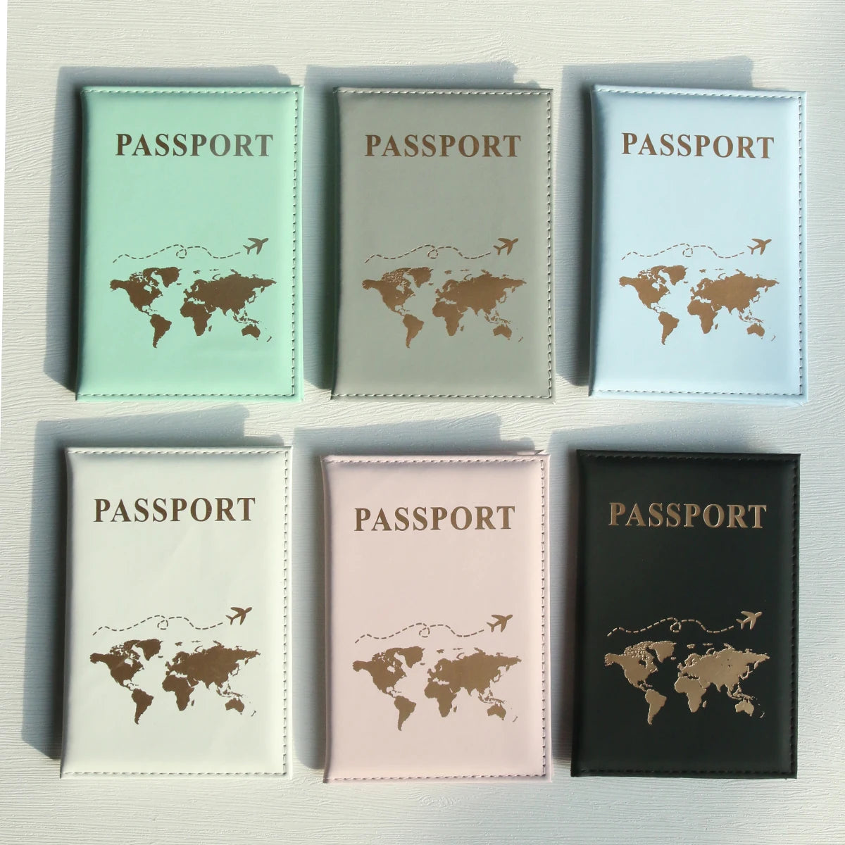 Ein Set aus fünf Reisepasshüllen in verschiedenen Grüntönen, Grau und Rosa, jeweils mit Weltkarten-Design.