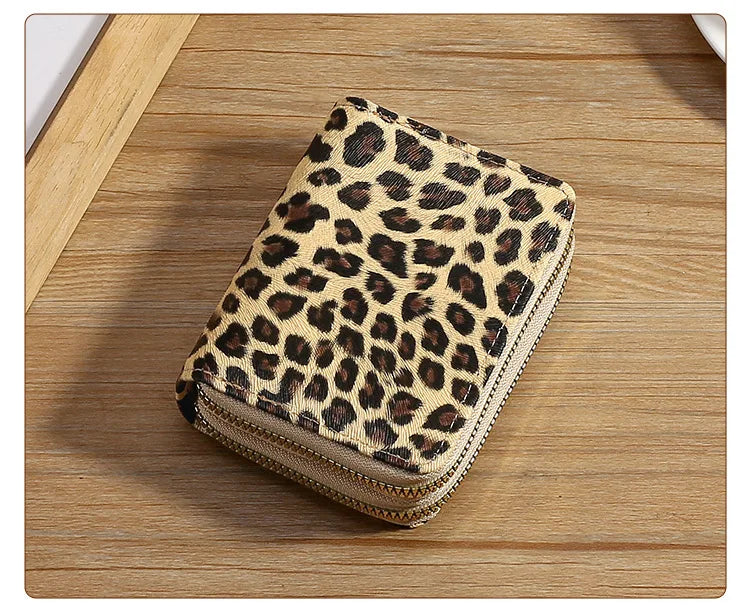 A beige leopard print double zipper wallet resting on a wooden surface.