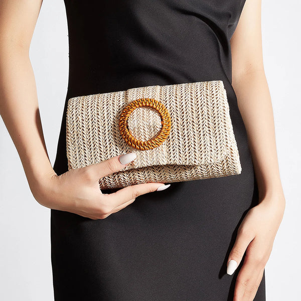 A woman holds a woven straw envelope clutch with an orange beaded strap against a black dress.