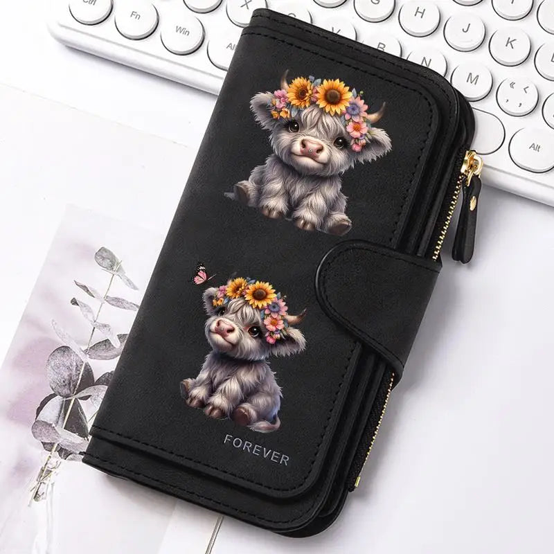Black zippered wallet featuring a small, fluffy Highland cow print charm on a white background.
