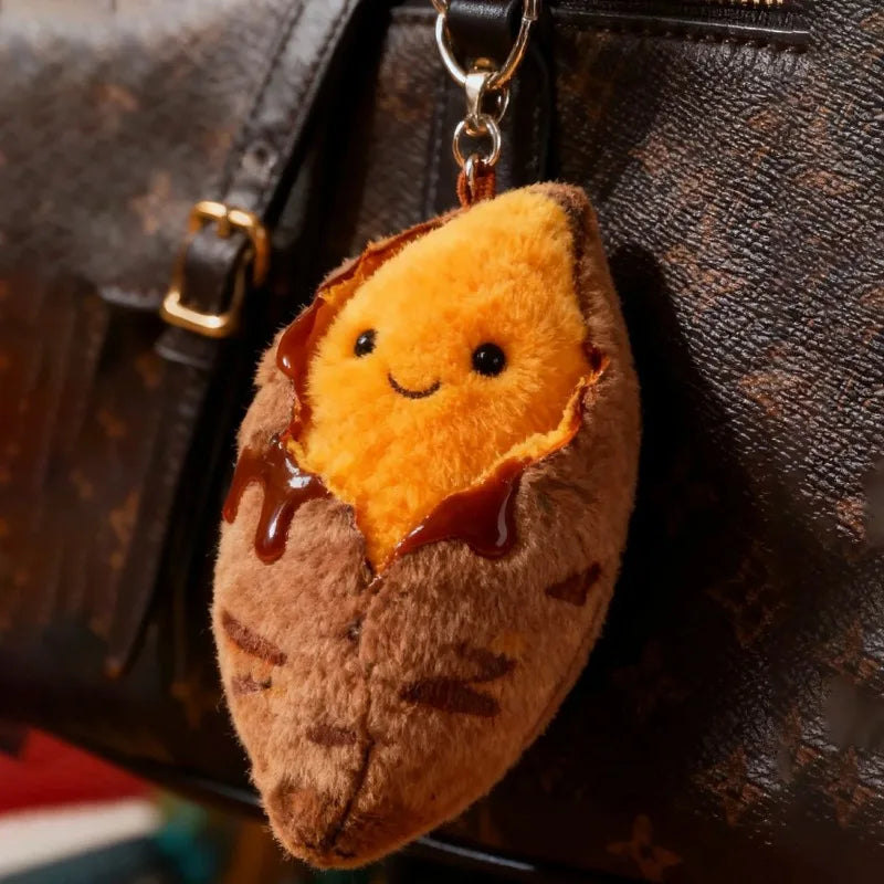 A fluffy orange roasted sweet potato plush keychain hanging from a leather bag.