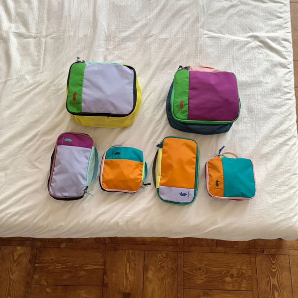 A set of colorful waterproof travel toiletry bags in shades of purple, green, yellow, and orange resting on a white sheet.