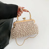 A beige pearl embellished crossbody shoulder bag held by a hand wearing red nail polish.